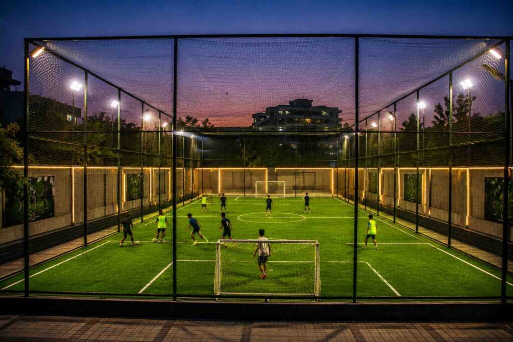 Kids playing football on a modern synthetic turf ground with floodlights during evening time in India.