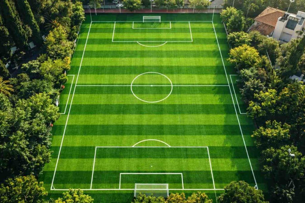 Artificial football turf installation on sports ground with green grass and white football field markings.